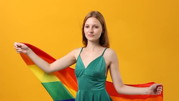 Young Beautiful Woman of Caucasian Ethnicity Cute Smiling with LGBT Flag on Yellow Pastel Background