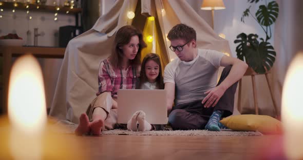 Mother Father and Adorable Child Sitting Near Toy Wigwam Using Laptop