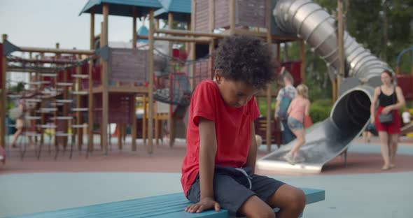 Sad Afroamerican Preschool Boy Sitting Alone on Bench on Playground