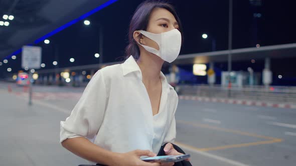 Asian business girl arrive destination wear face mask stand outside look smart phone wait car .