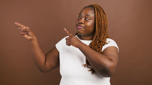 Positive African American Lady Looking Aside and Pointing with Fingers at Free Space Brown Studio