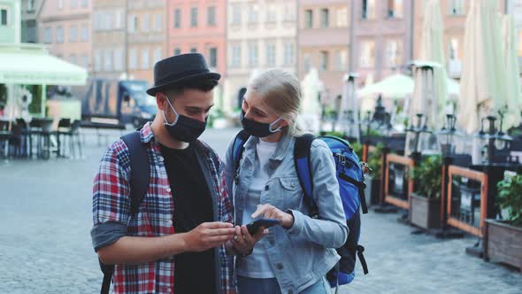 Man and Woman in Protective Masks and with Bags Using Smartphone