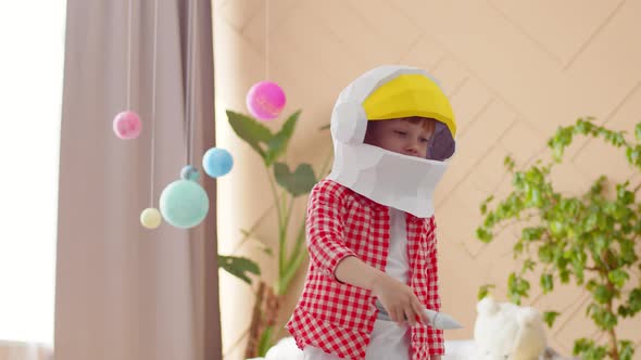 Girl in a white T-shirt, shirt and paper astronaut helmet plays with a toy rocket flying