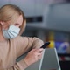 A Woman in a Protective Mask is Waiting for Her Flight in the Airport Terminal Using a Smartphone - VideoHive Item for Sale