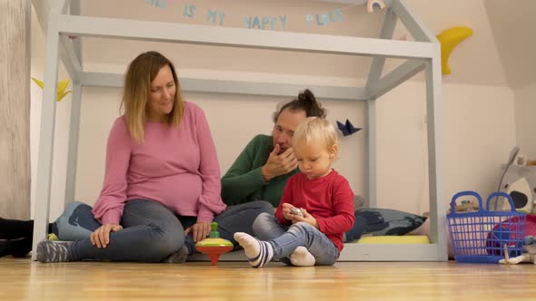 Father and mother showing spinning toy to Infant son at children room.