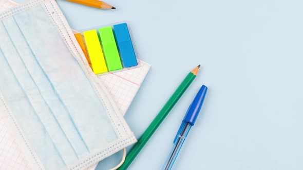 School Supplies with a Notepad Lie on a Pastel Blue Background with a Medical Mask