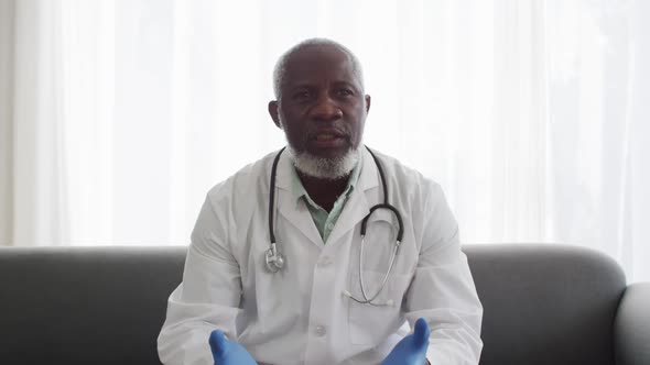 Portrait of male african american doctor wearing surgical gloves talking while having a videocall