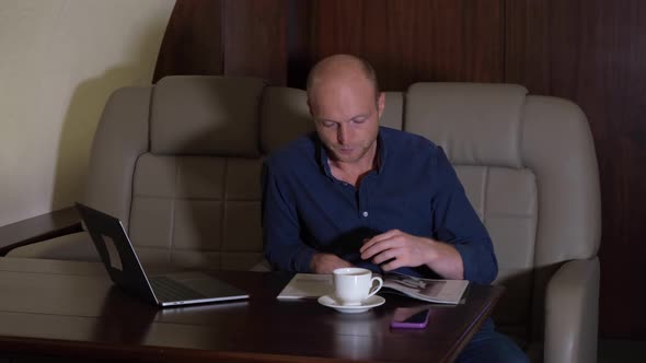 A young Businessman Drinks Coffee and Reads a Magazine, he is Sitting in his Business Jet