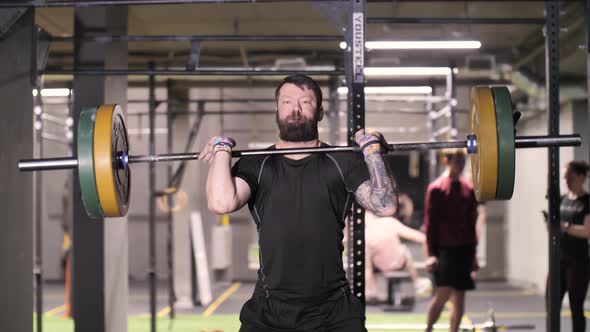Brutal Strong Man Does Overhead Lift with Barbell Athletic Training in Gym