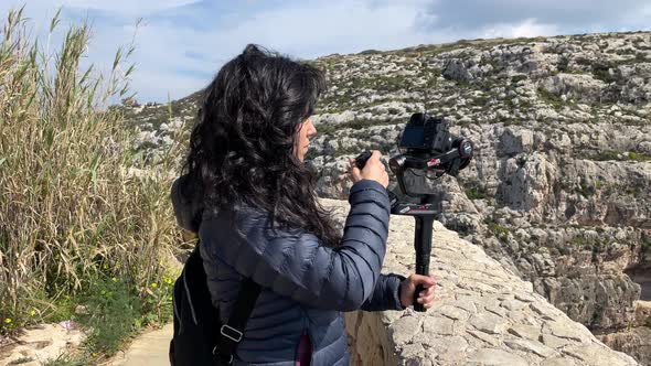 Young woman filming with her camera greats during an outdoor adventure with rocky landscape in the b