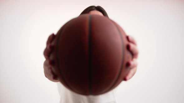 European Bearded Man with Long Hair Hiding Behind Basketball Ball and Looking at Camera From Time to