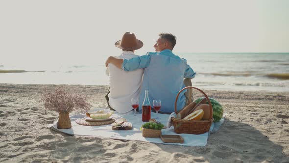 Homosexual Lgbt Couple Gay Men Having Picnic at Beach Sitting on Blanket and Embracing Looking to