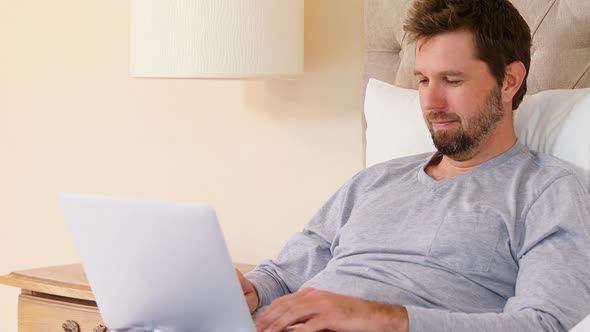 Young man sitting on bed using his laptop in the bedroom at home 4K 4k