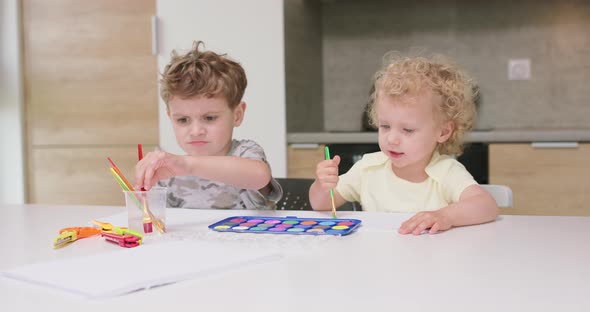 Brother and Sister Draw Watercolors While Sitting at the Table Father Puts a Glass of Water for the