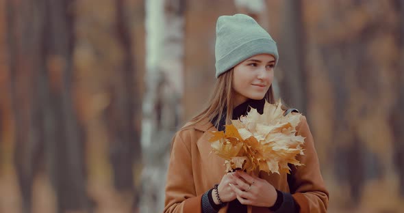 Portrait of a Girl in the Autumn Forest with a Bouquet of Orange Leaves