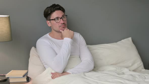 Pensive Middle Aged Man Sitting in Bed Thinking 