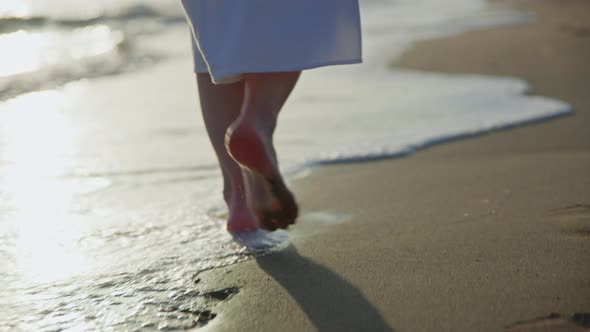 Barefoot girl in a white dress walking along the seashore