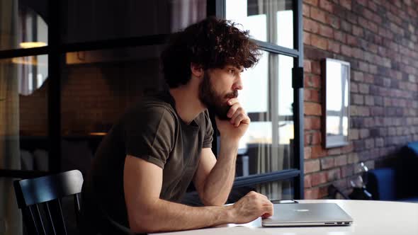 Thoughtful Young Man Tapping His Fingers on Lid of Closed Laptop Sitting at Desk at Home Office