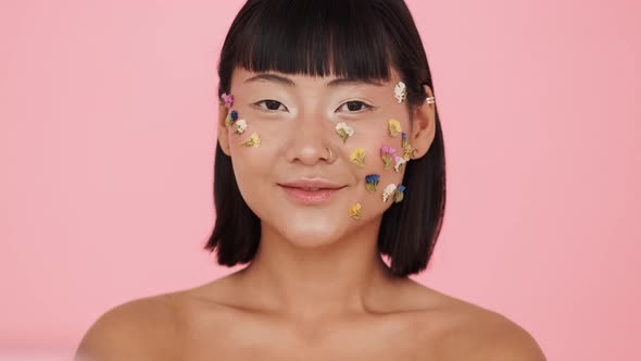 A beautiful brunette asian woman posing with colorful flowers on her face