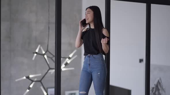 Cheerful Young Woman Standing in Glass Office Talking on the Phone Laughing