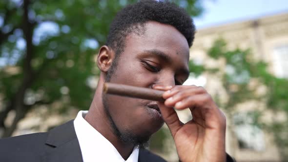 Closeup Face of Satisfied Wealthy African American Man in Elegant Suit Smelling Cigar Looking at