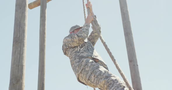 Caucasian male soldier in uniform climbing down rope on military obstacle course in sun