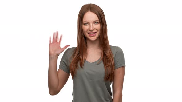 Portrait of Pretty Redhead Woman 20s Smiling and Greeting Person with Waving Hand Isolated Over