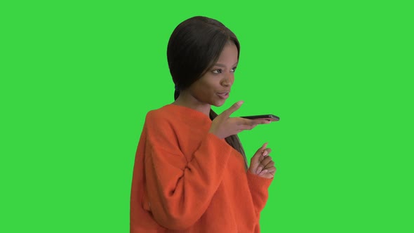 Pretty African American Woman in Bright Jumper Dictating Message Using Her Phone on a Green Screen