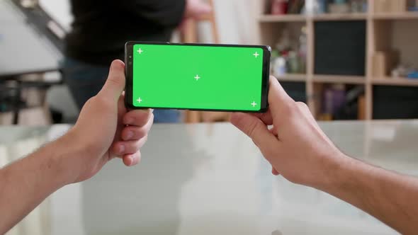 Mans Point of View Holding a Smartphone Horizontally with Green Screen on