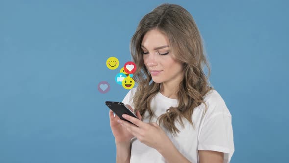 Young Woman Using Smartphone Isolated on Blue Background, Flying Smileys, Emojis and Likes