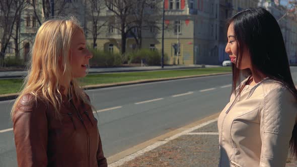 A Young Caucasian Woman and a Young Asian Woman Shake Their Hands and Talk in a Street