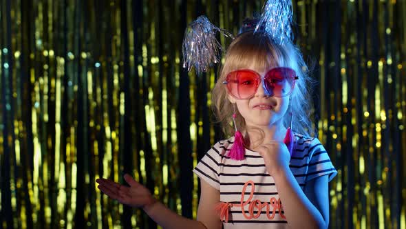 Trendy Girl in Stylish Glasses Standing on Blue Neon Lights Pointing at Blank Space Agree Sign