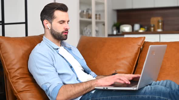 A Focused Man Wearing Casual Shirt Using a Laptop Sitting at Home