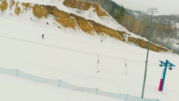 People Ski Down Wide Snowy Trail with T-bar Lift Aerial View