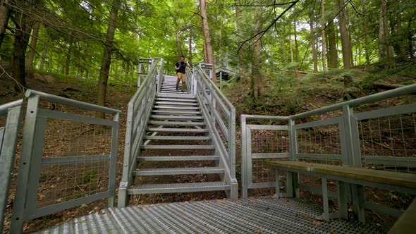 Male hiker with backpack quickly descends steep metal staircase in forest landscape, walking towards
