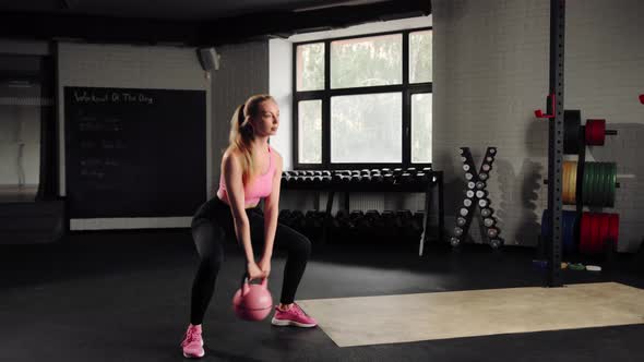 Attractive young beautiful woman doing cardio exercise and squatting with kettlebell in gym