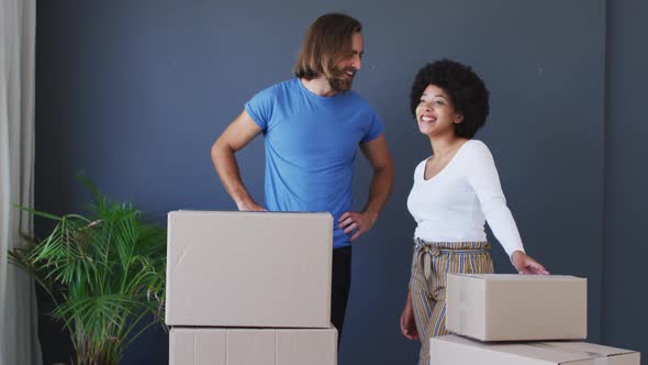 Mixed race couple standing in between cardboard boxes at new apartment house