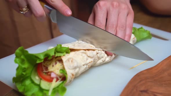 Women's Hands Cut in Half Pita with Vegetables and Cheese on a Cutting Board