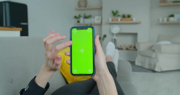 Woman at Home Lying on a Couch Using Smartphone with Green Mock-up Screen, Doing Swiping, Scrolling