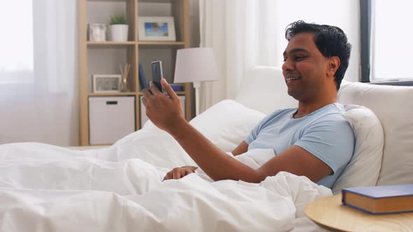 Happy Indian Man with Smartphone in Bed at Home