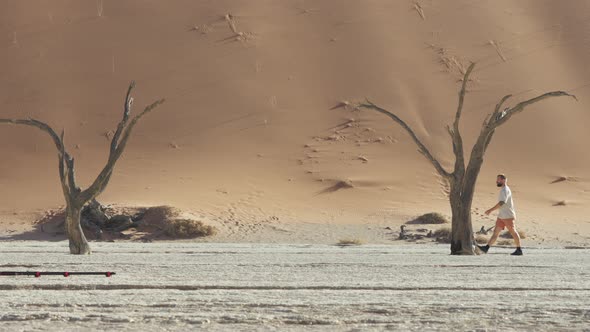 Young Man With Camera Walking In The Deadvlei, Clay Pan With Dead Camelthorn Trees Near Sossusvlei.