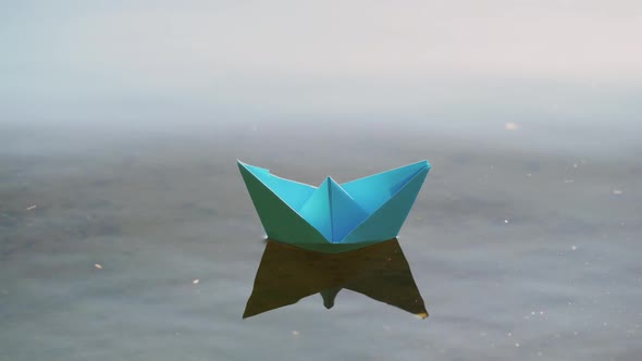 Blue paper boat sailing on water on romantic sunset. Origami.