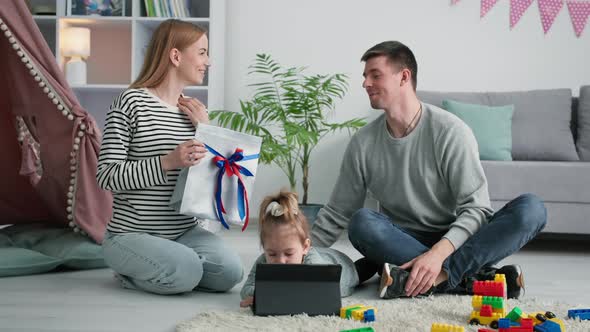 Fathers Day Loving Wife Gives Her Husband Present While Female Child Plays on Tablet During Family