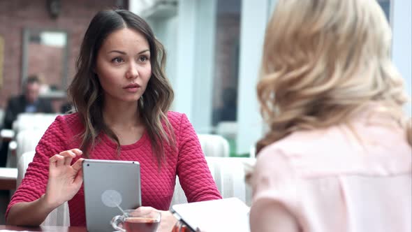 Two Women Sitting in Rustic Cafe Looking at Pictures on Digital Tablet