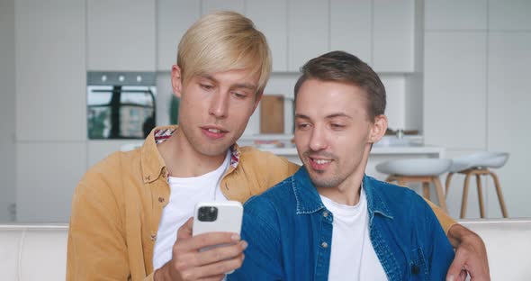 Happy Men Homosexual Couple Sit at Home Together on Their Sofa and Using Smartphone