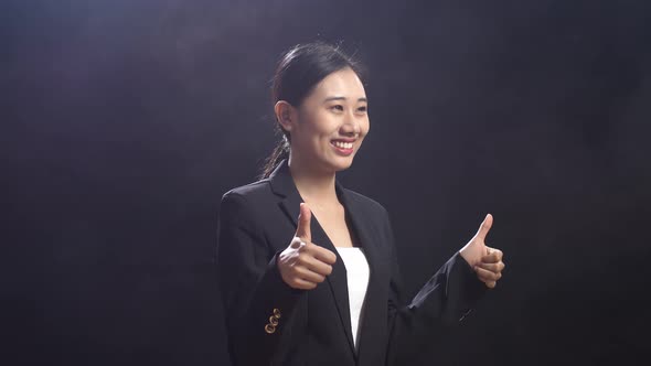 Smiling Asian Speaker Woman In Business Suit Showing Thumbs Up Gesture While Standing On Stage