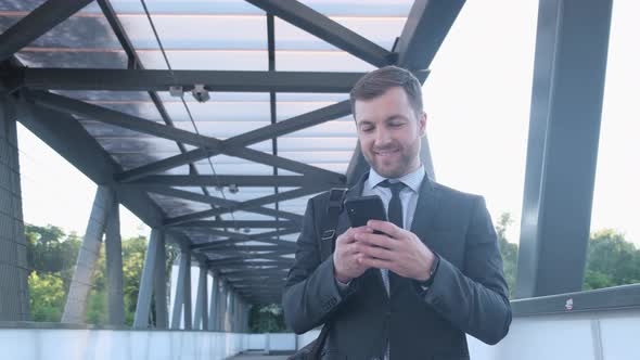 Confident Smiling Man Reads a Message on the Phone in the Morning