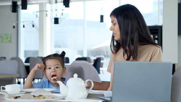 Businesswoman Mom Gives Pizza to Child Sitting at Table