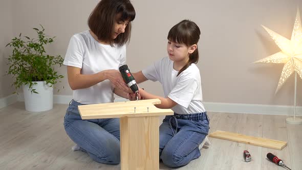 Happy Family Mother and Daughter Assembling Wooden Furniture Together with Screwdriver
