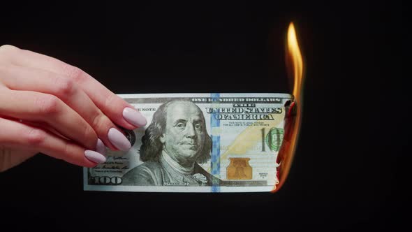 Woman Holding Burning American Hundred Dollar Banknote on Black Background